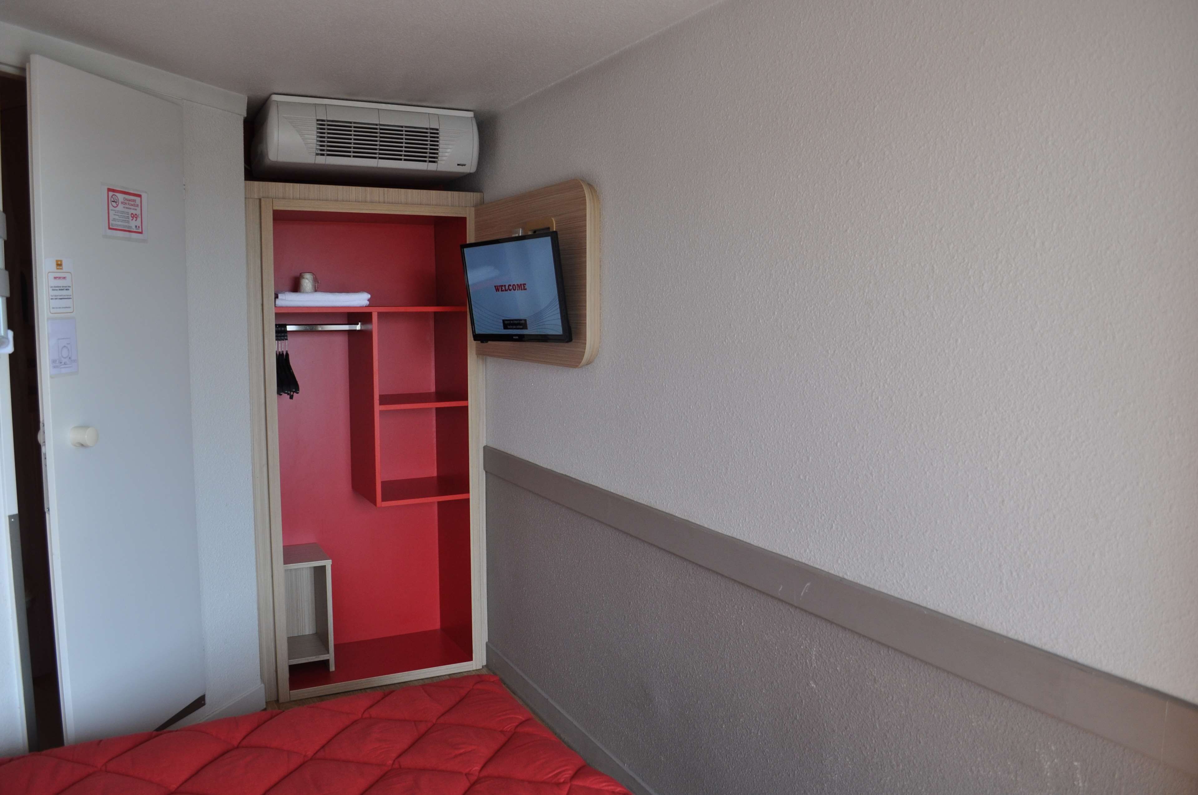 Een hotelkamer met een rood bed, een rode kledingkast, een televisie aan de muur en een airconditioning.