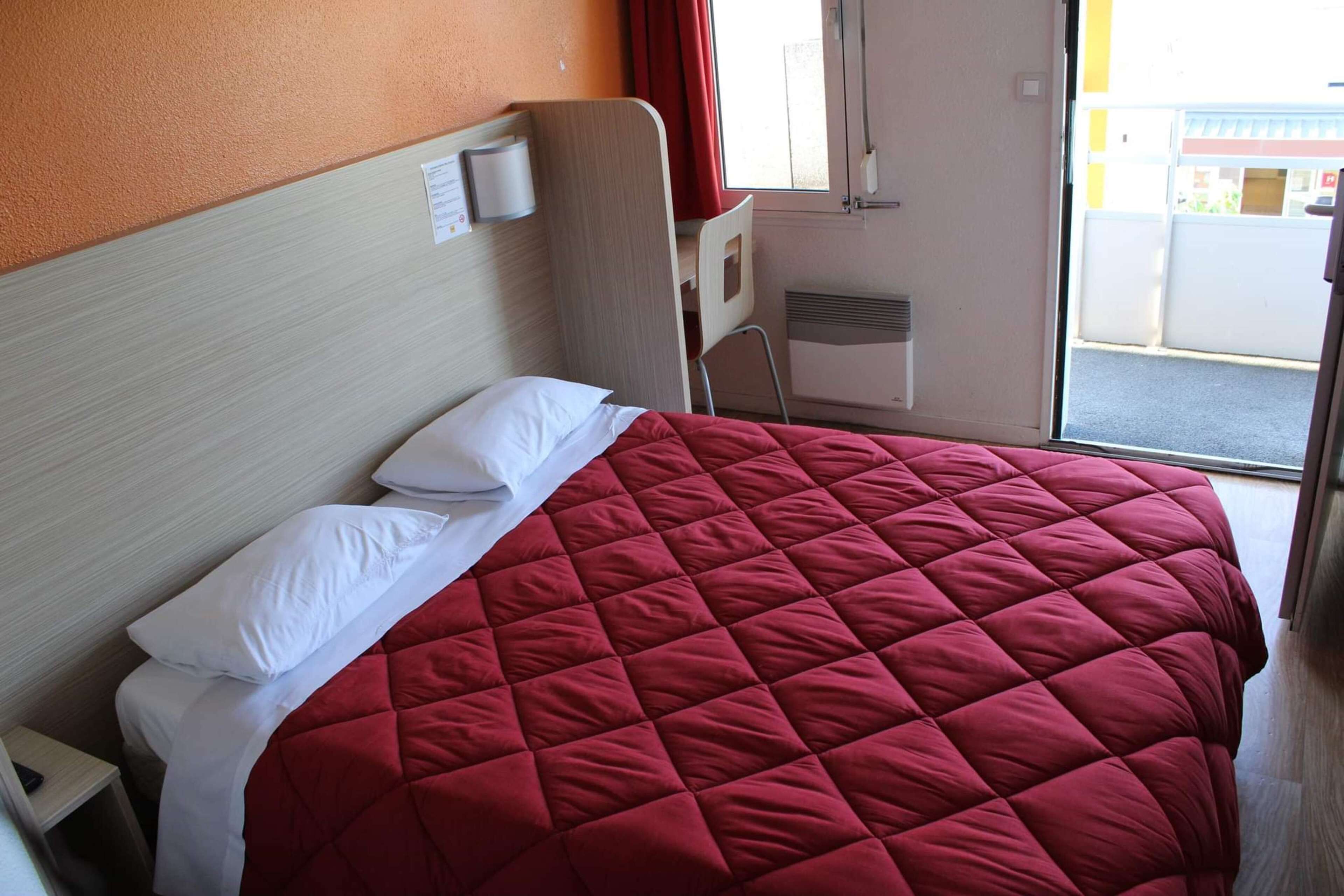 A hotel room with a bed, a chair, a window, and a door.