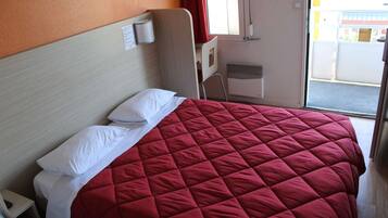 A hotel room with a bed, a chair, a window, and a door.