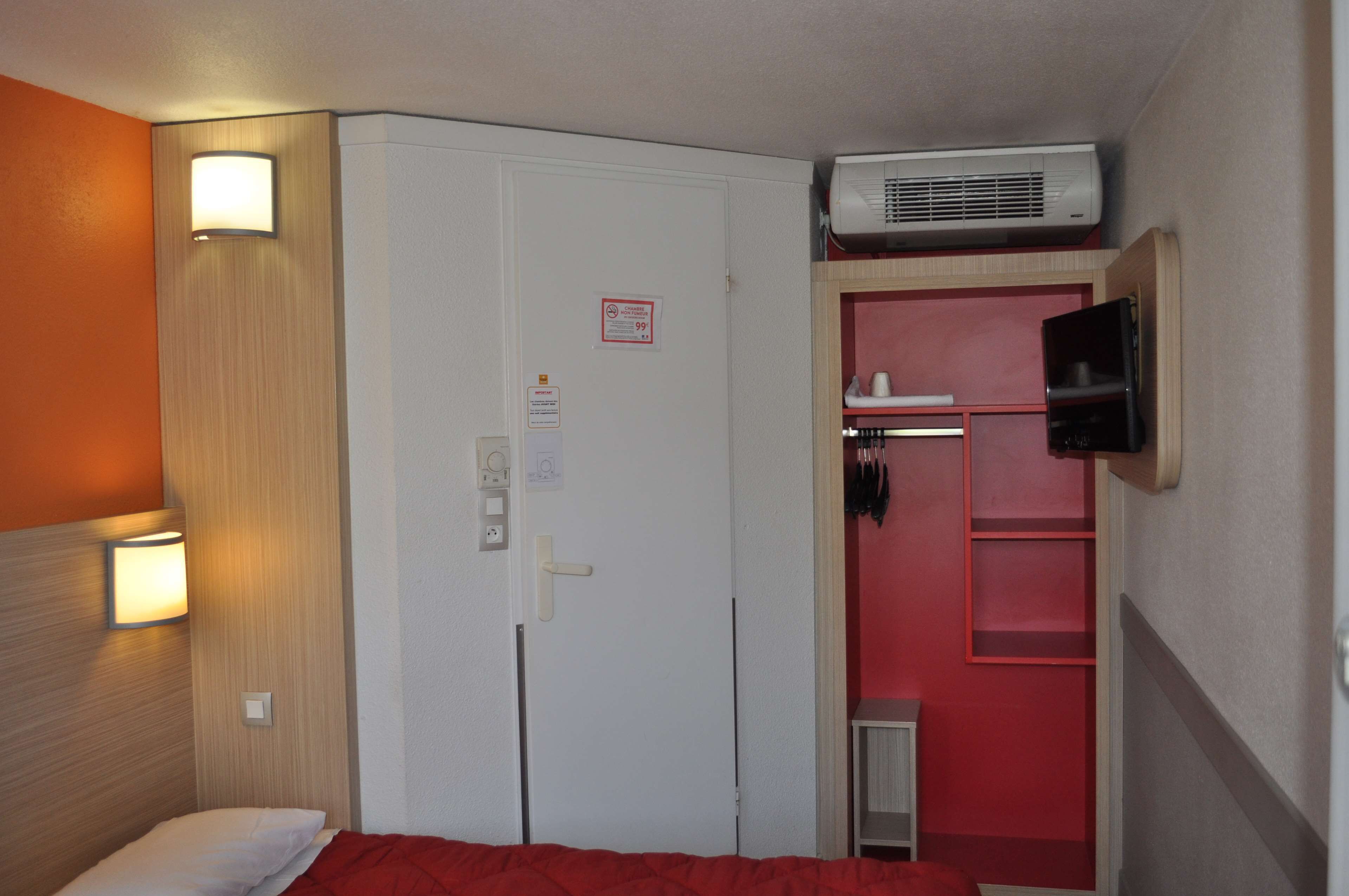 Habitación de hotel con una cama, un armario, un televisor montado en la pared y un calentador sobre el armario.
