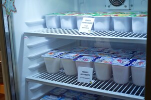 Un refrigerador lleno de productos lácteos varios, incluyendo recipientes etiquetados de compota de manzana y yogur de frutas.