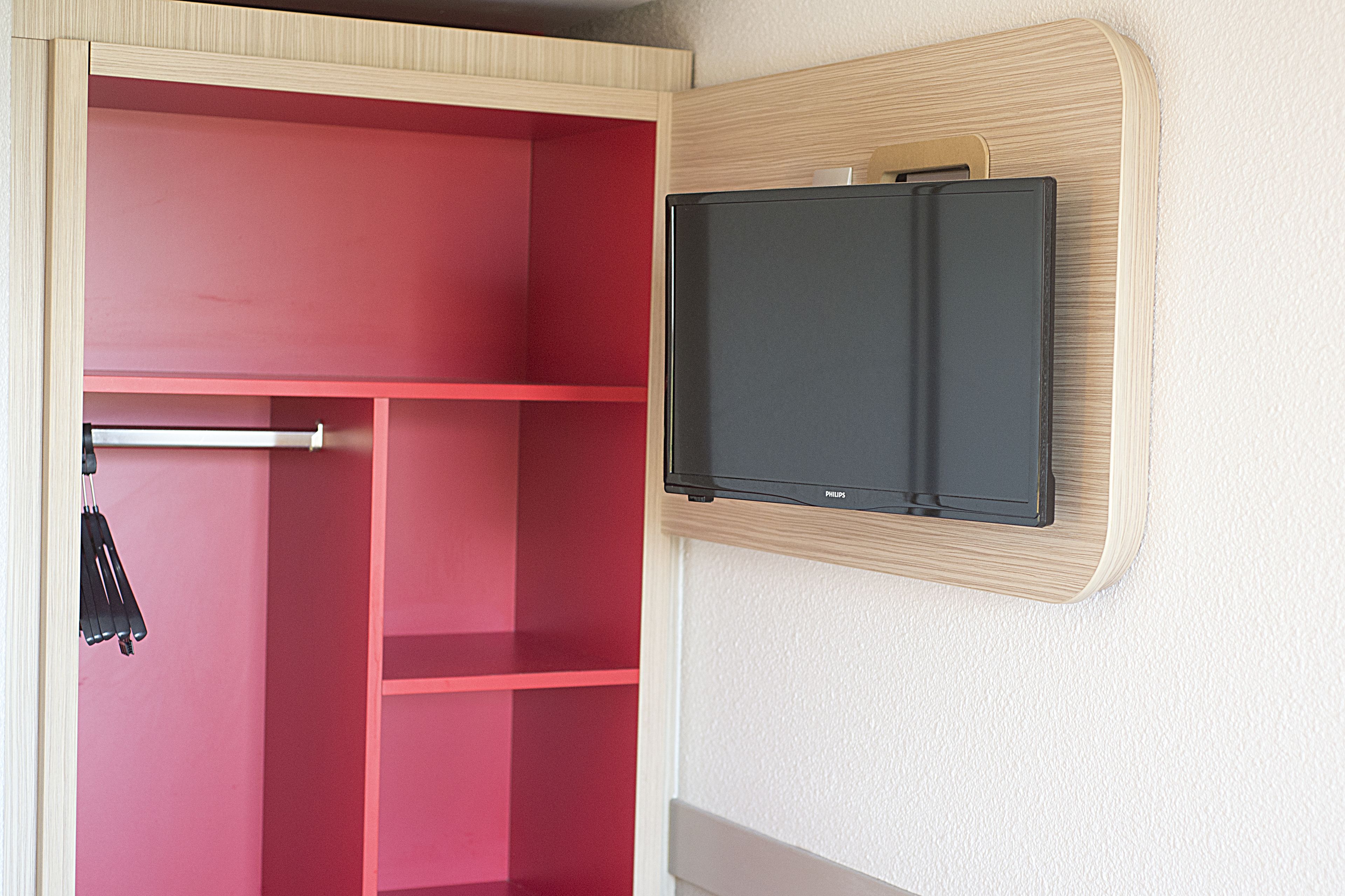 A room with a red wardrobe and a mounted television.