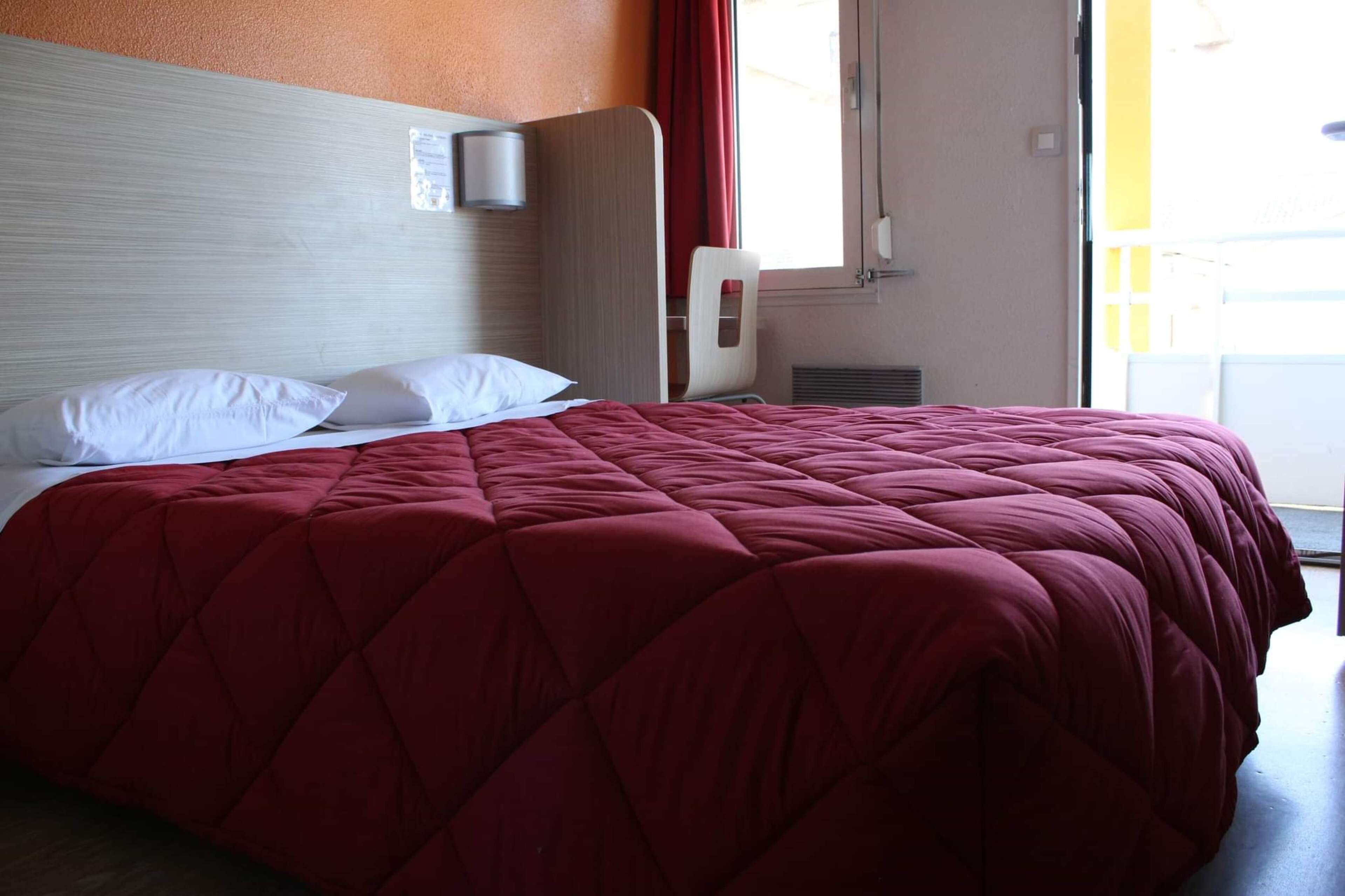 Habitación de hotel con una cama grande, cabecera, ventana con cortinas rojas y puerta que da a un área exterior.