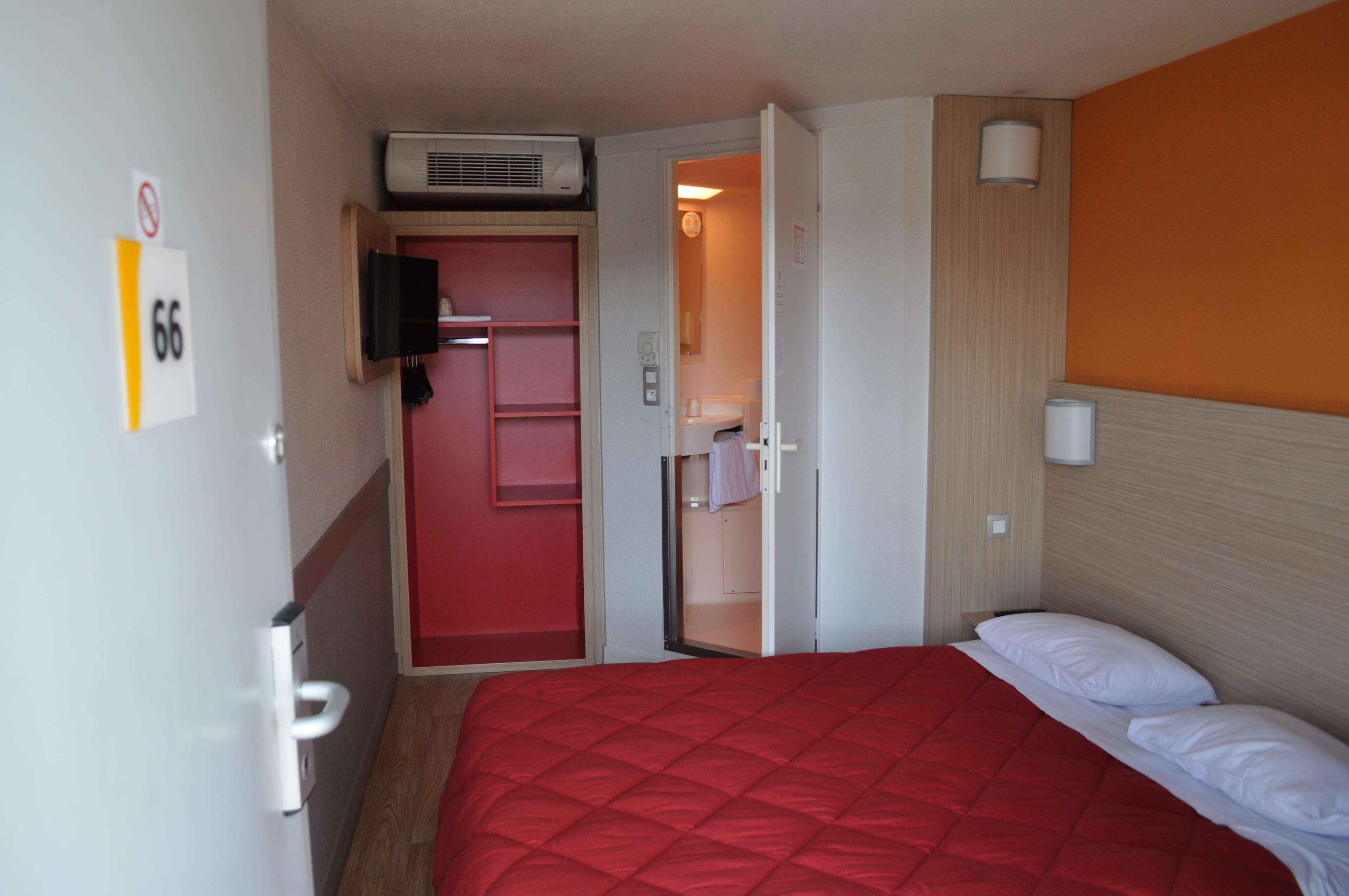 A hotel room with a red bed, a closed door, and a wall-mounted TV.