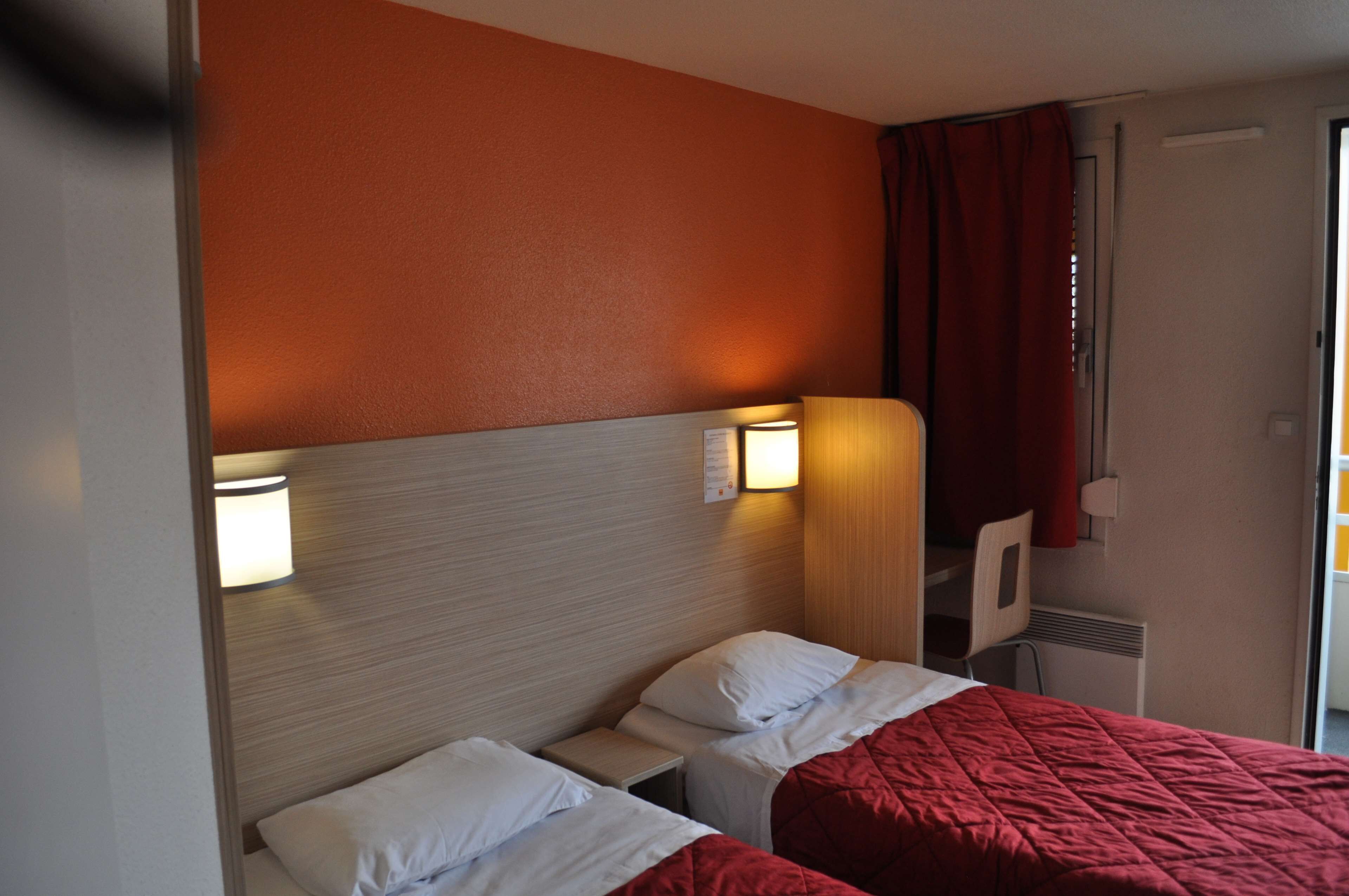 A hotel room with two beds, a wooden headboard, and a red curtain.