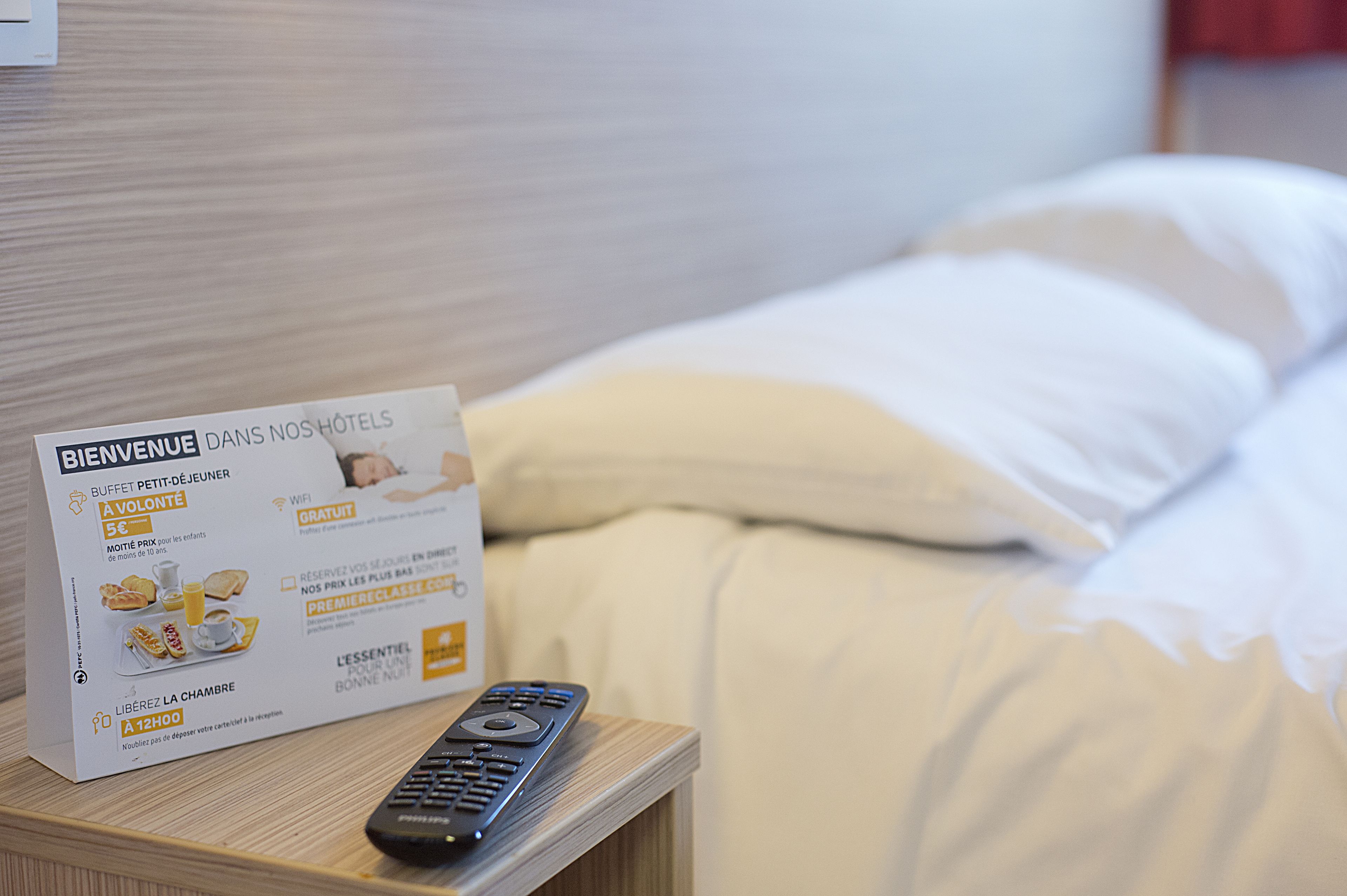 Une chambre d’hôtel avec un lit, une télécommande et un panneau de bienvenue posé sur la table de chevet.