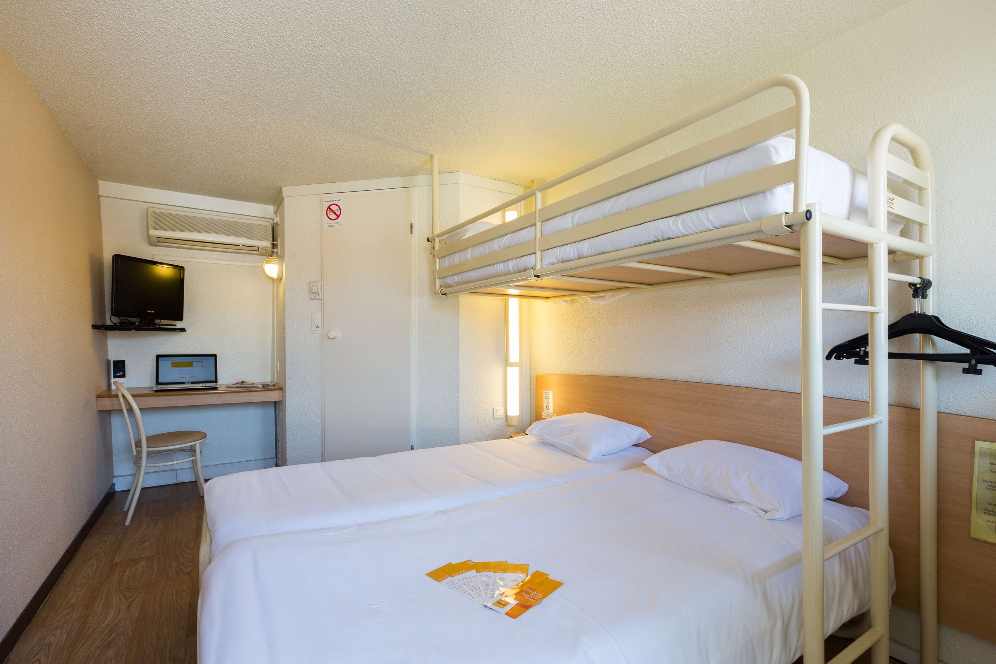 Een hotelkamer met een stapelbed, een bureau met een computer en een televisie.