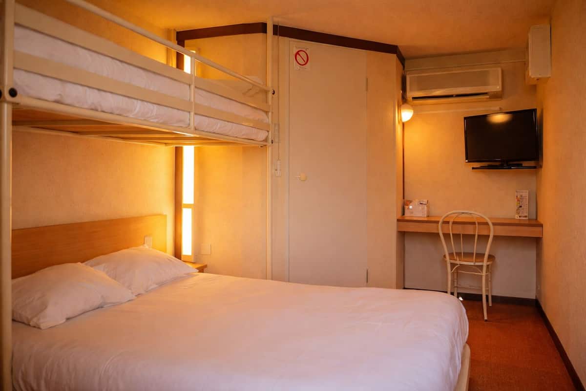 Hotelkamer met een stapelbed, een bureau met stoel, een televisie en een deur met een rookvrij bordje.