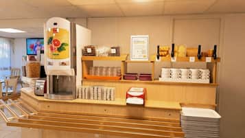 Uma estação de café à disposição dos hóspedes, com máquina de café, dosadores de temperos e diversos copos descartáveis.
