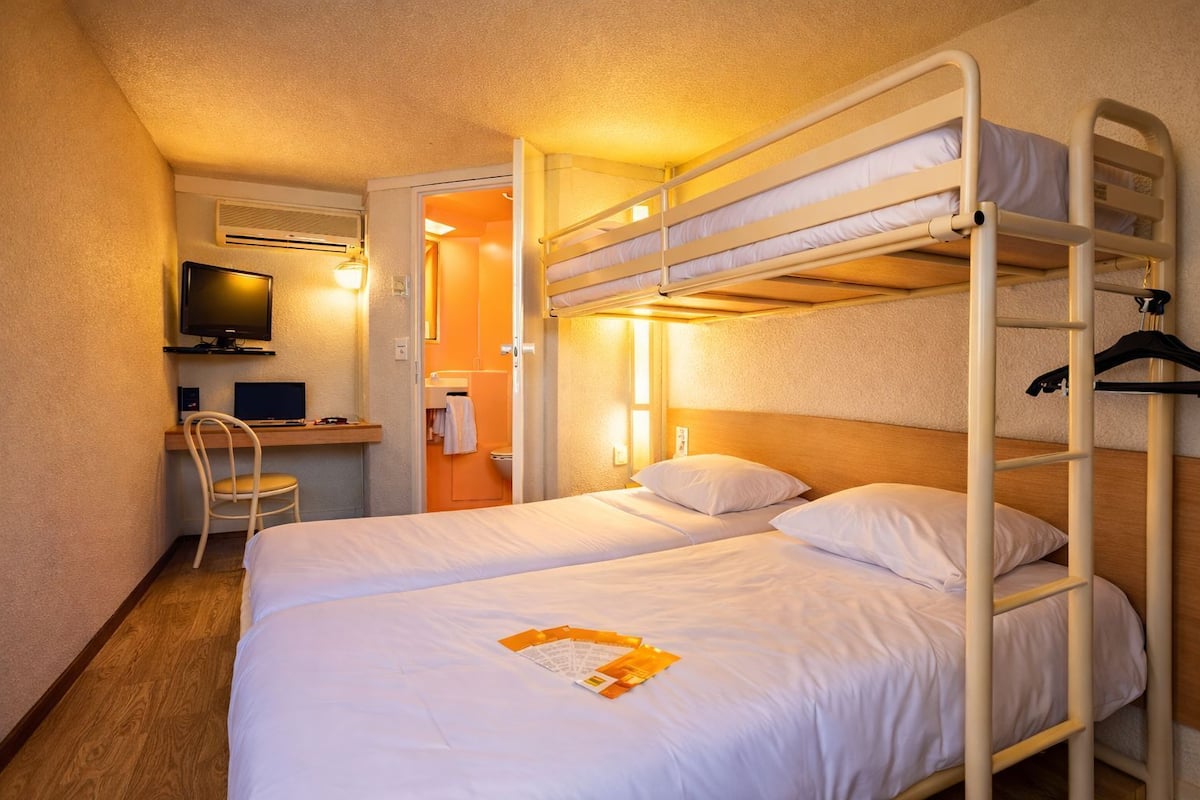 Een slaapkamer met een stapelbed, bureau, stoel en televisie.