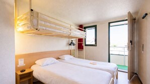 Une chambre avec deux lits simples, une table de chevet en bois, un lit superposé, une fenêtre avec vue et une porte donnant sur un balcon extérieur.