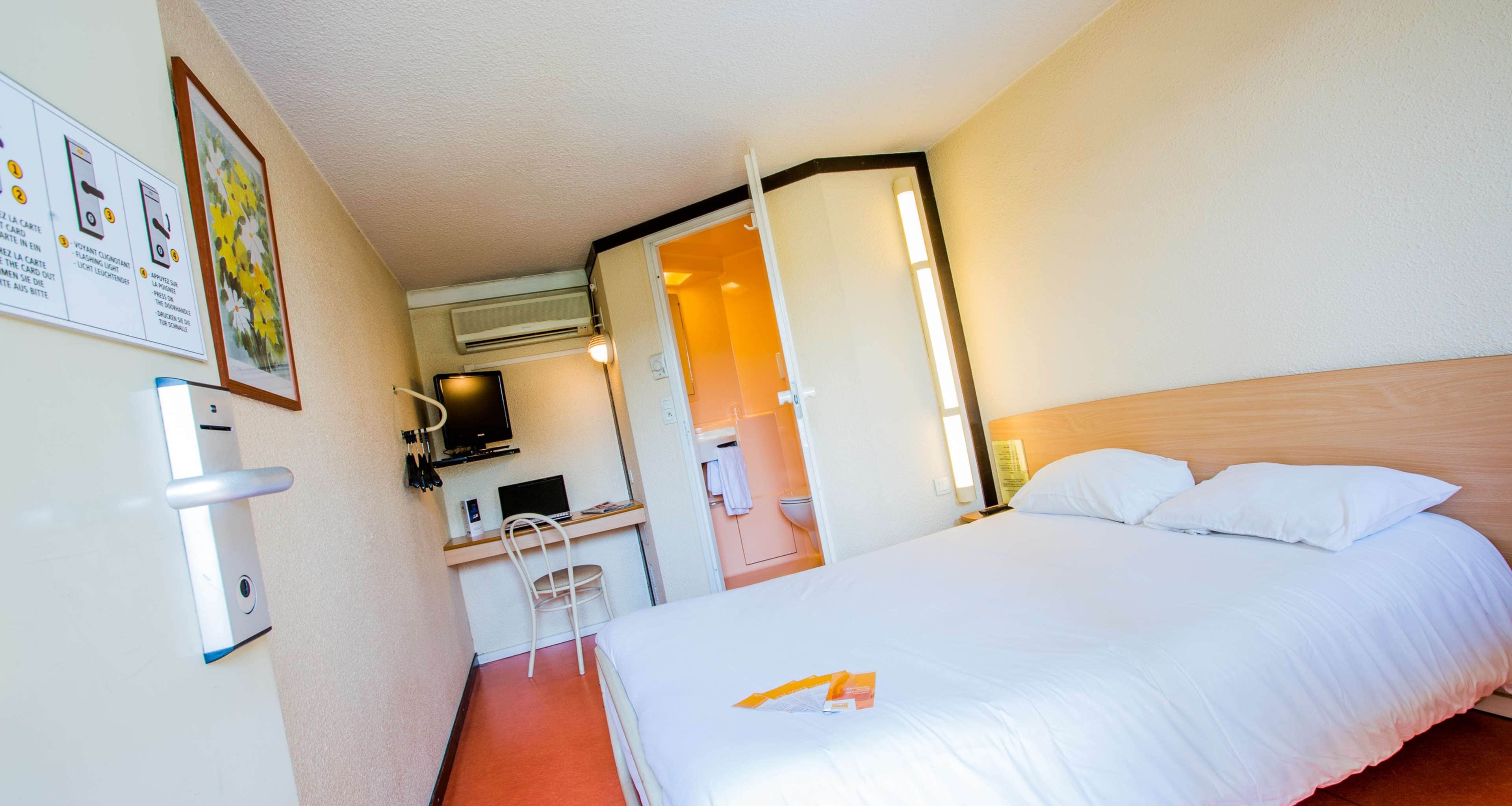 Una habitación de hotel con una cama, un escritorio con una computadora y un equipo de aire acondicionado.