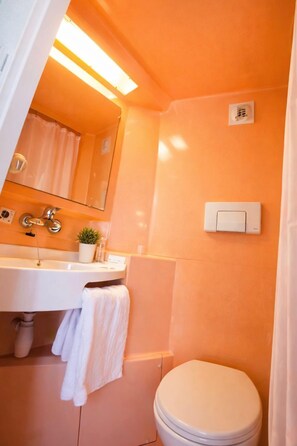 Une salle de bain avec un lavabo blanc, un miroir, des toilettes et un interrupteur sur le mur.