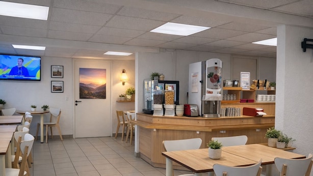 Un café avec des tables et des chaises en bois, un appareil à café et un écran de télévision diffusant un programme d’information.