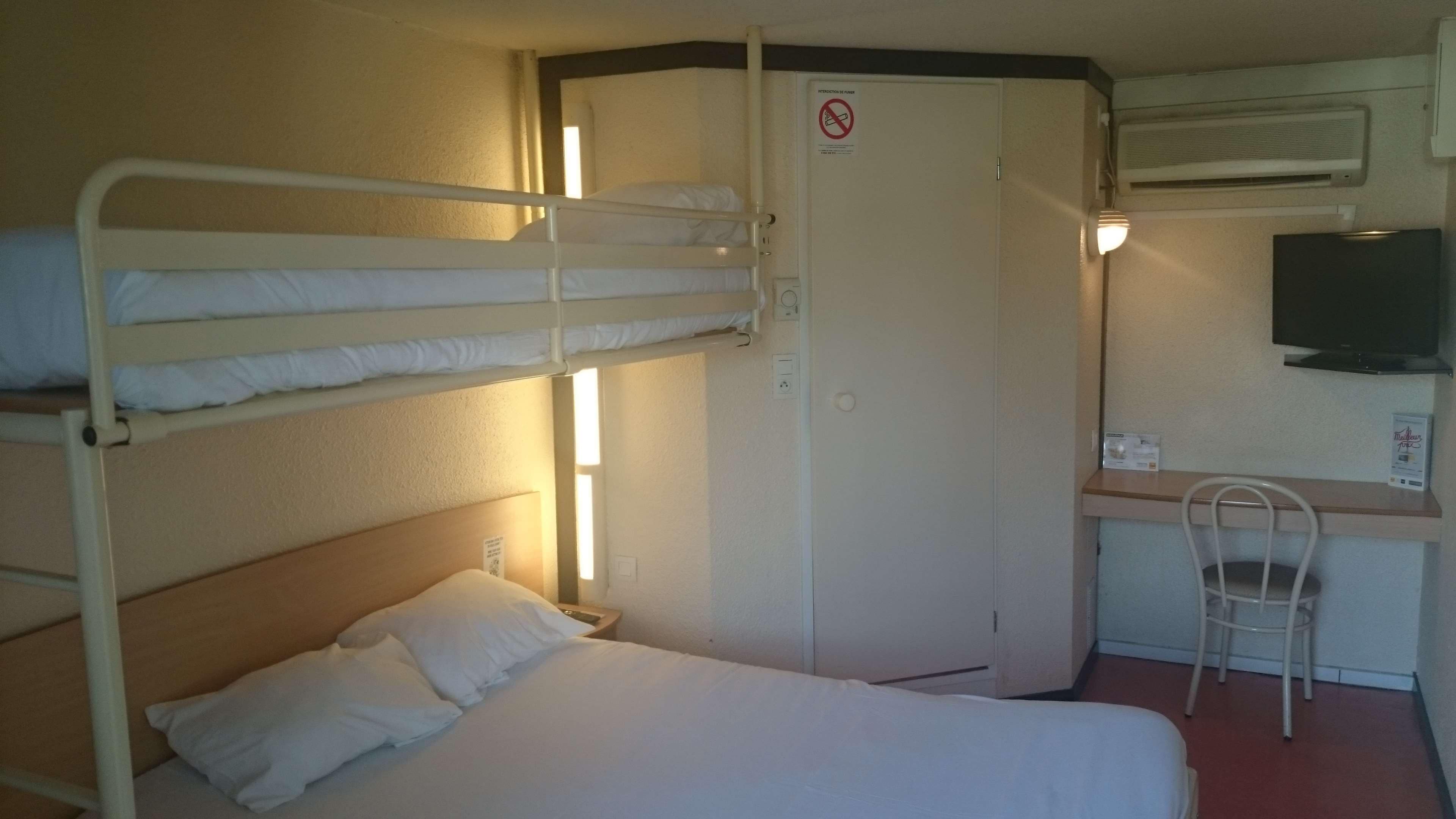 Habitación con literas, escritorio, silla, televisión y un cartel de prohibido fumar.