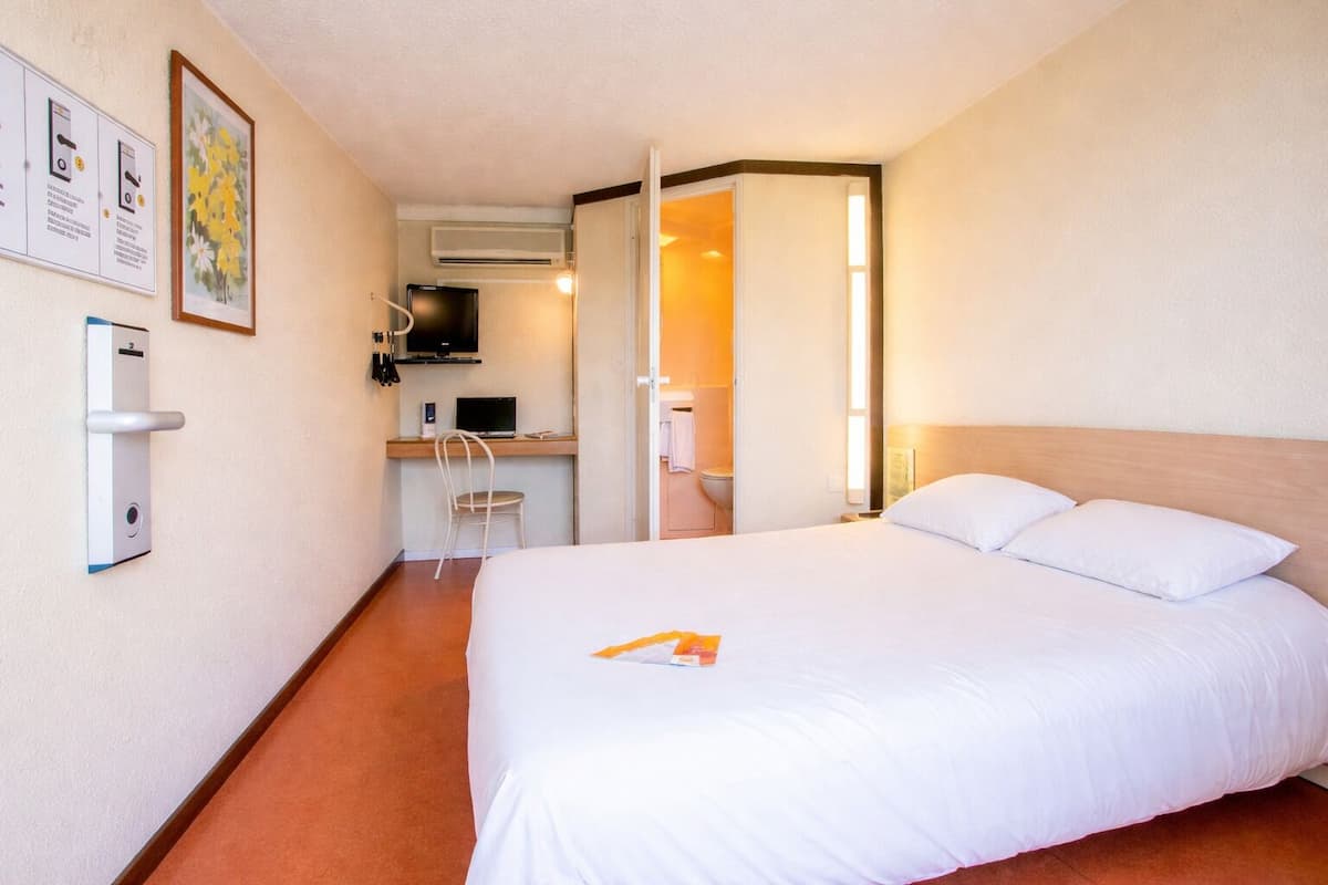 Een hotelkamer met een bed, een bureau met stoel, een televisie en een badkamer zichtbaar door een geopende deur.