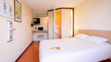 Habitación de hotel con cama, escritorio con silla, televisor y baño visible a través de una puerta abierta.
