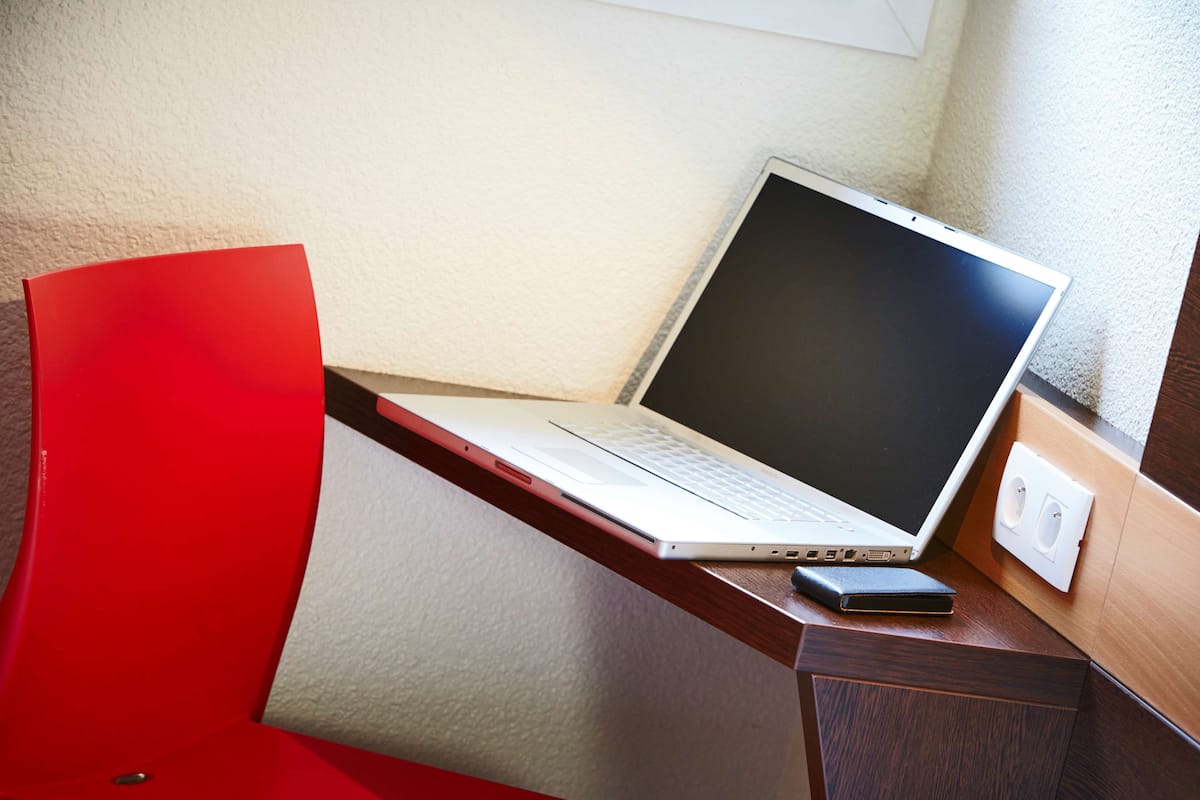 Een laptop op een houten bureau met een rode stoel.