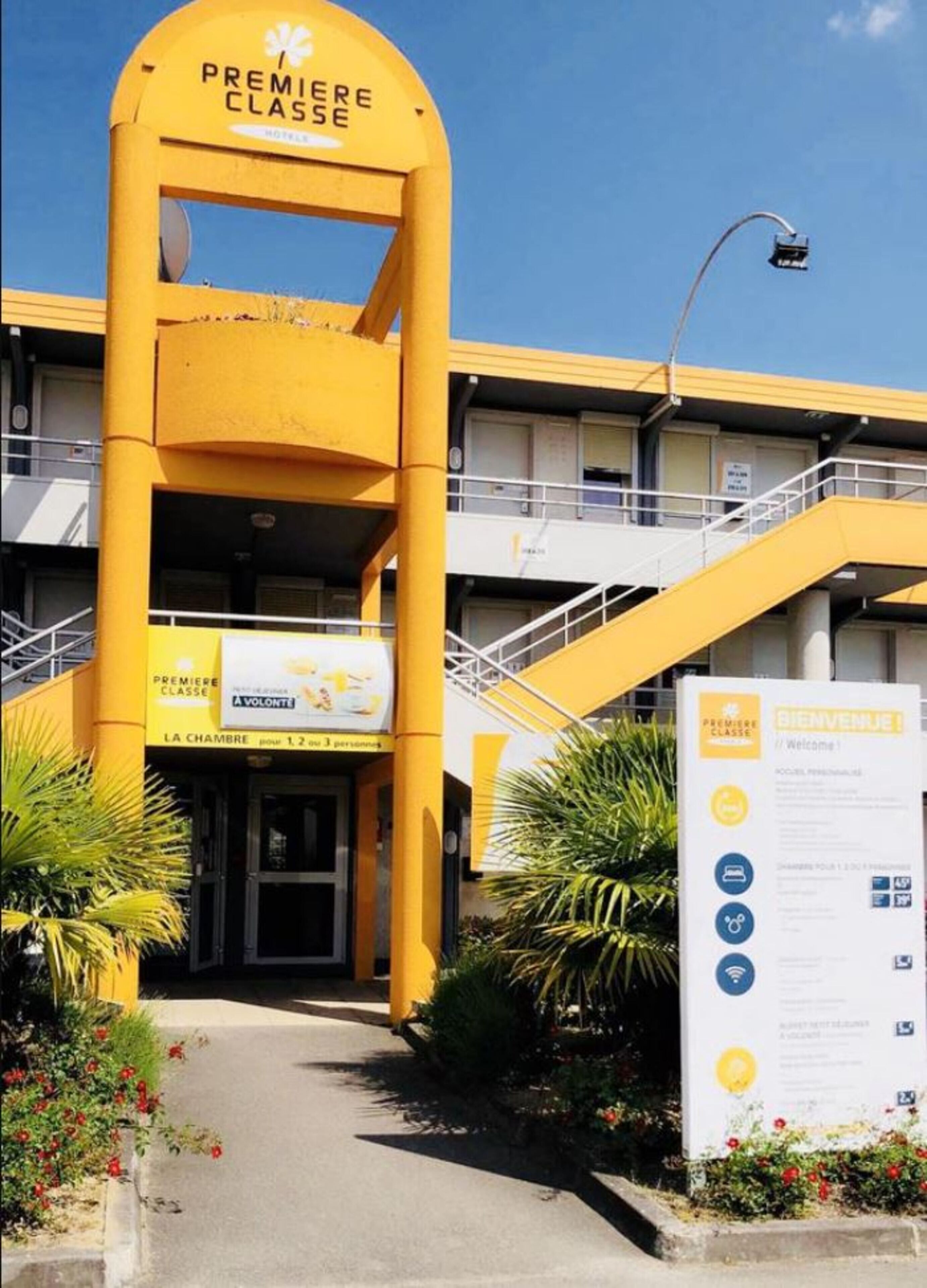 A hotel entrance with a prominent yellow archway labeled "PREMIERE CLASSE" and a welcome sign with amenities listed.