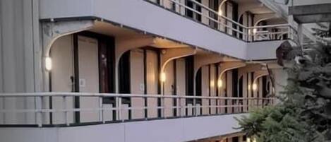 Un hôtel à plusieurs étages doté de balcons, d’une galerie couverte et d’un petit jardin.