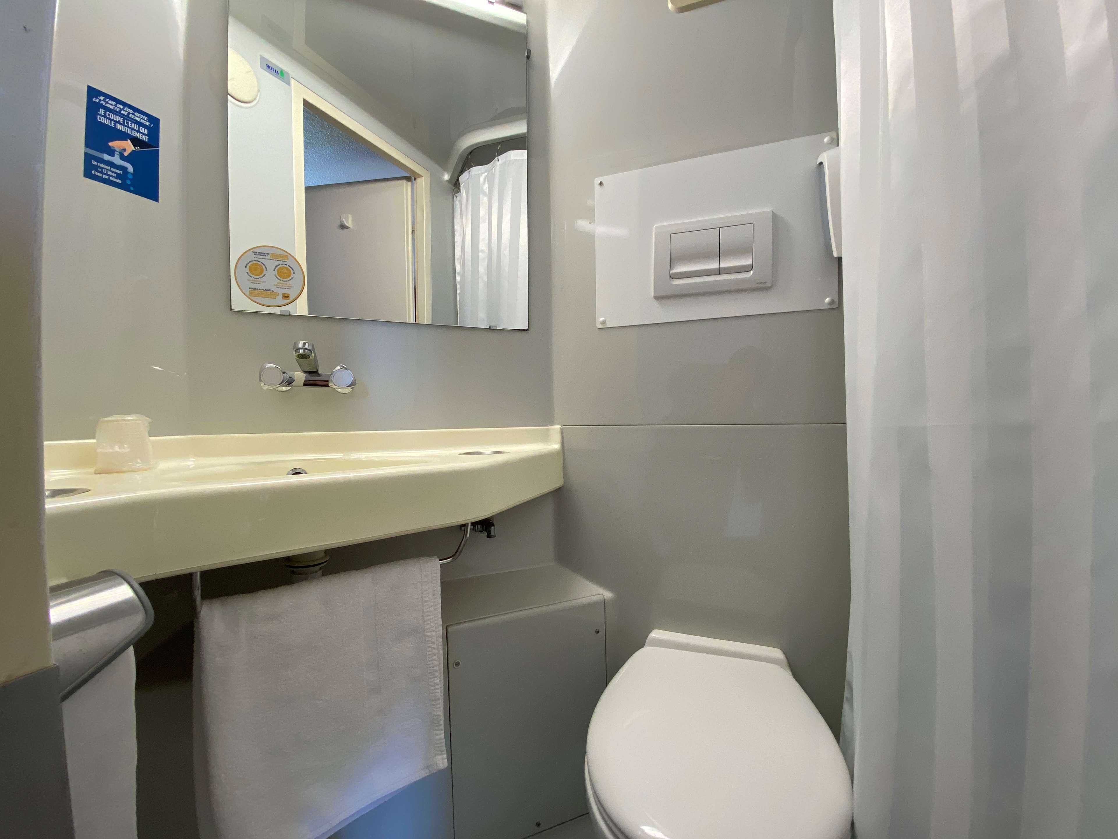 Un baño con lavamanos blanco, espejo e inodoro. Hay una toalla colgada en la pared y una cortina de ducha.