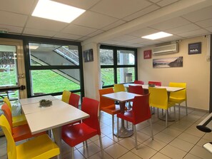 A dining area with multiple tables and chairs, large windows, and an air conditioning unit on the wall. - Premiere Classe La Rochelle Sud-Angoulins (Angoulins)