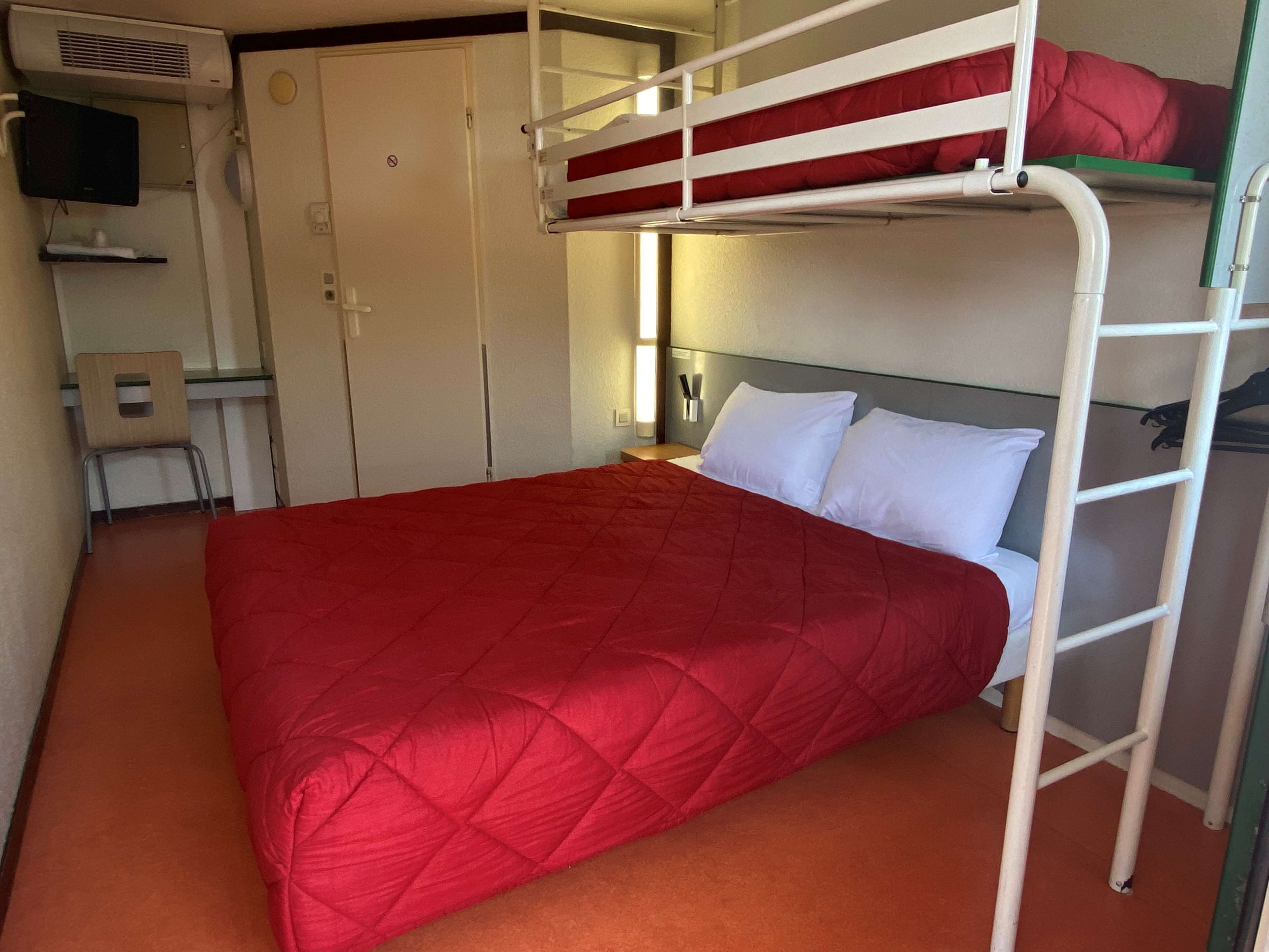 A bunk bed with a red quilt, a desk with a chair, a TV, and a wardrobe.