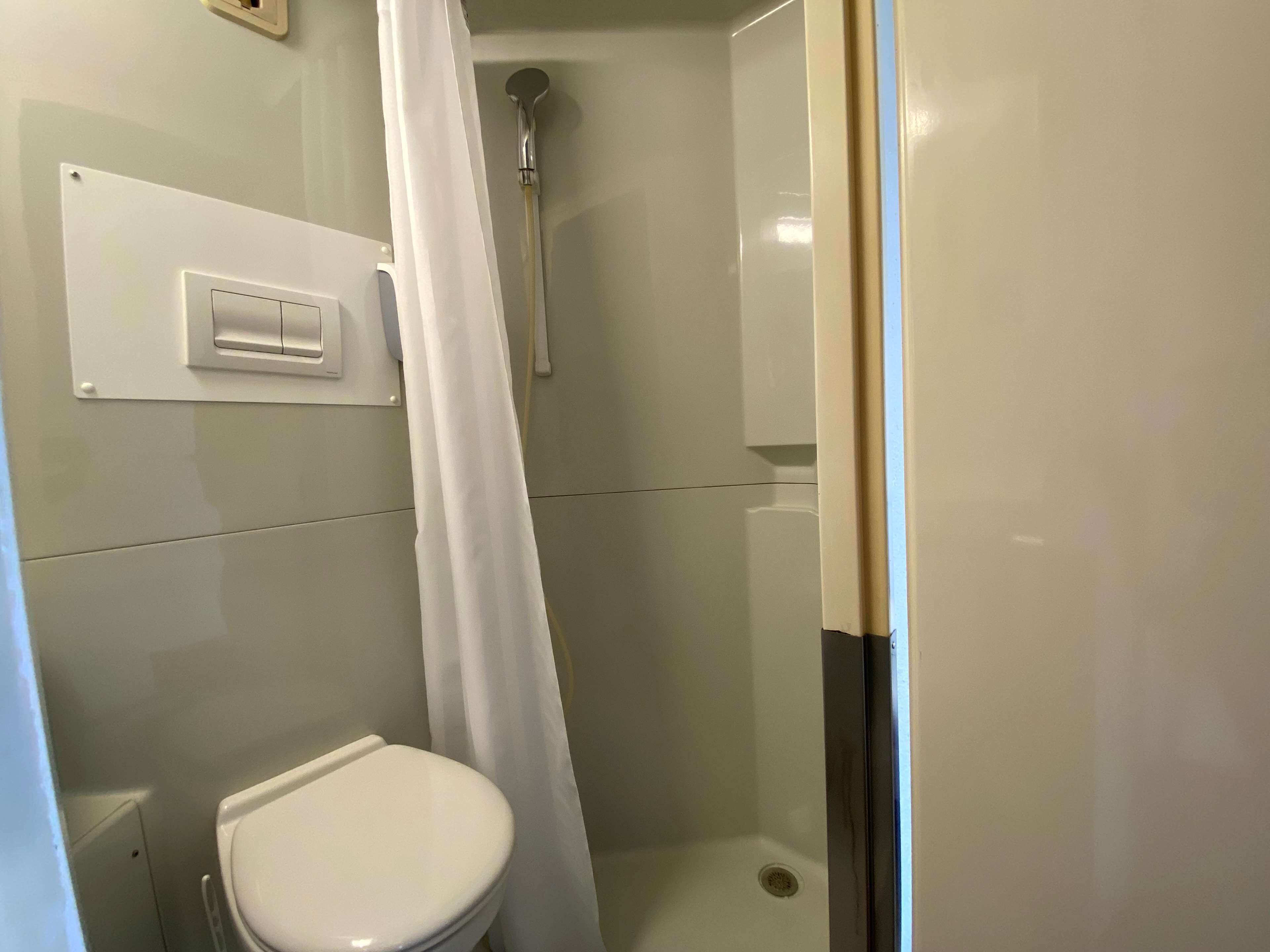 A small, enclosed shower area with a toilet and a control panel.