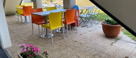 Un patio al aire libre con mesas y sillas, una planta en maceta y una jardinera.