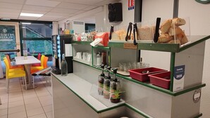 A café counter with a variety of food items, condiment dispensers, and a seating area with colorful chairs. - Premiere Classe La Rochelle Sud-Angoulins (Angoulins)