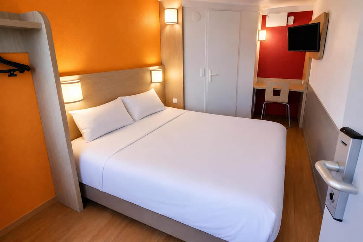 Una habitación de hotel con cama, escritorio, silla, televisor y puerta.