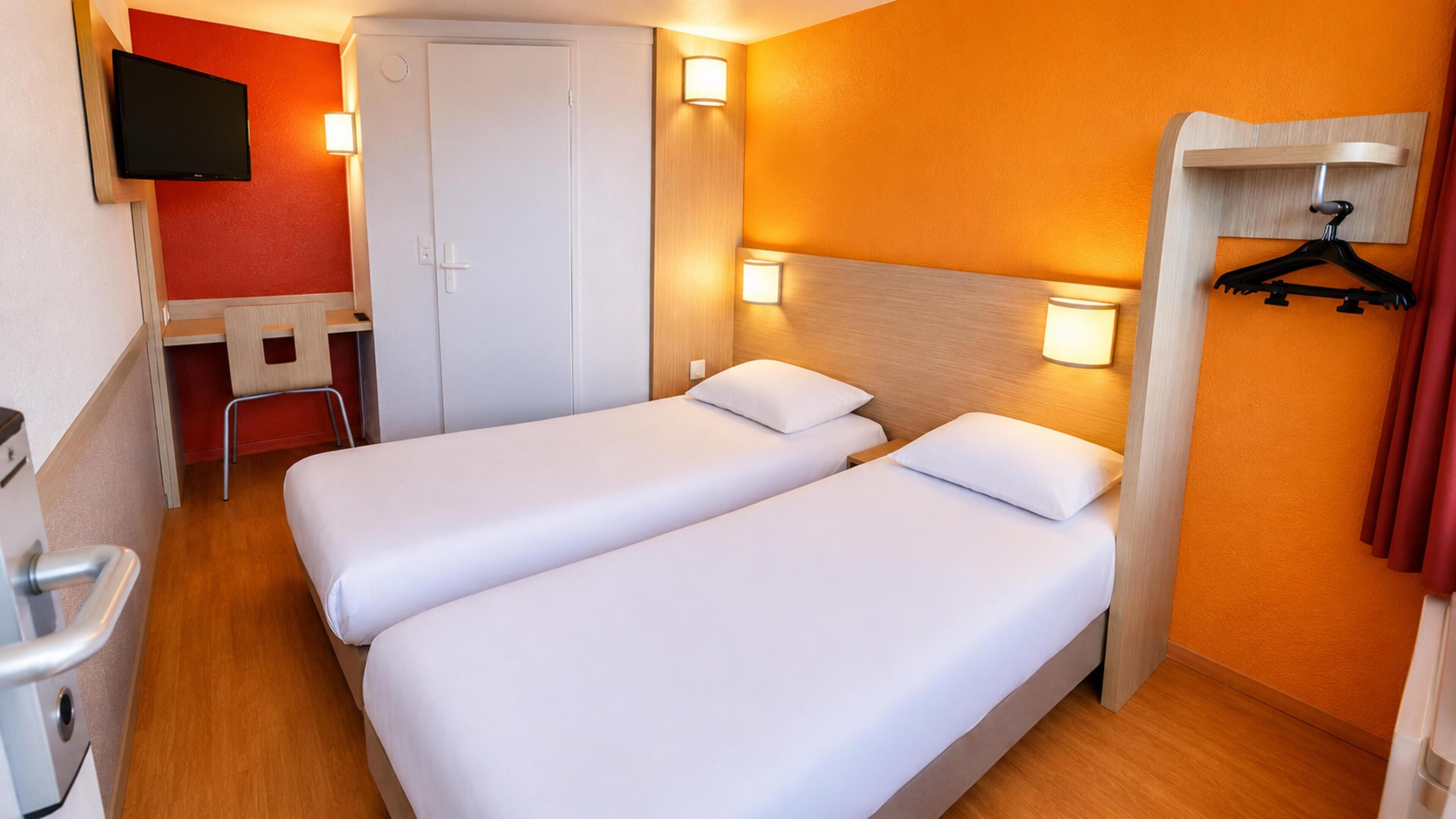 Hotellihuone, jossa on kaksi erillistä sänkyä, työpöytä, tuoli, televisio ja vaatekaappi, jossa on peili.