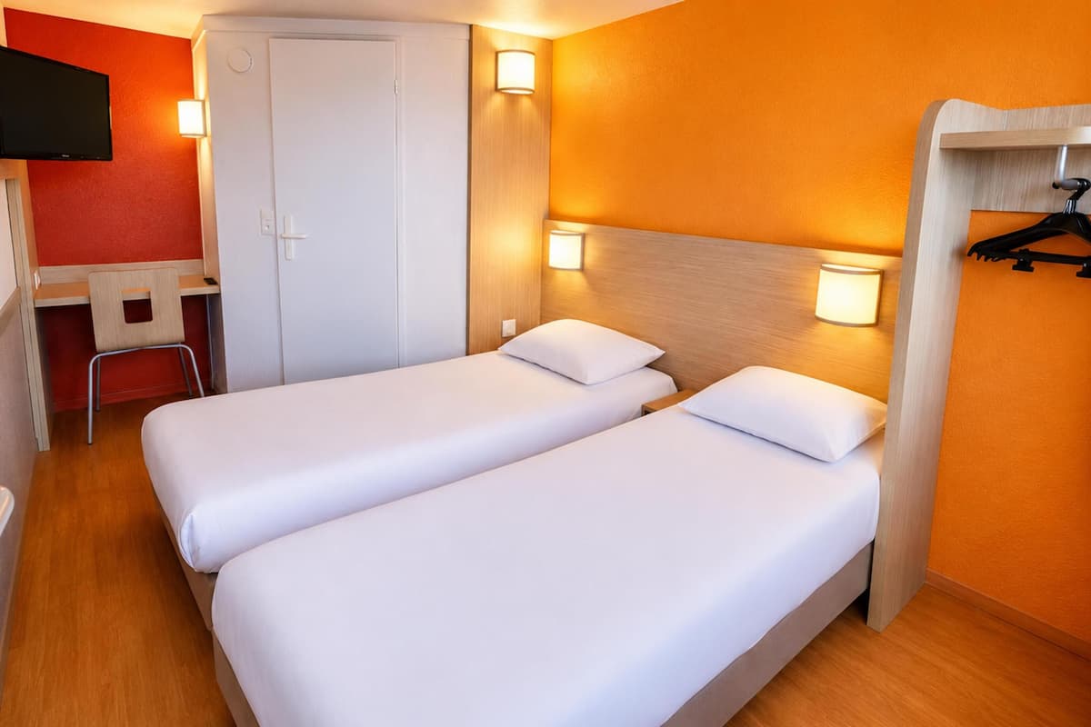 Una habitación de hotel con dos camas individuales, un escritorio, una silla, un televisor y un armario con espejo.