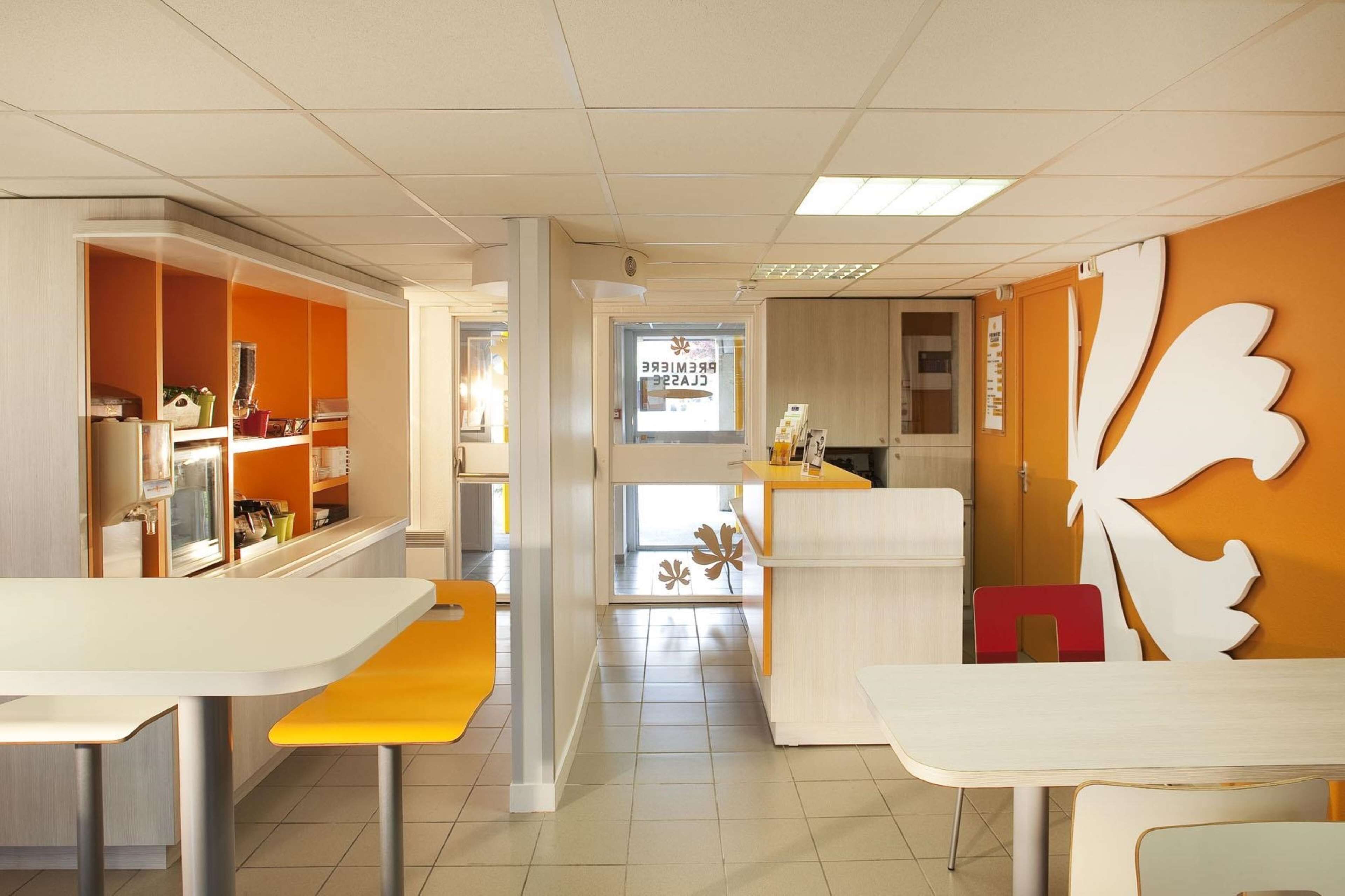 Een modern restaurantinterieur met wit en oranje decoratie, een centraal gelegen balie en een groot decoratief blad aan de muur.