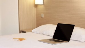 Habitación de hotel con cama, una laptop sobre la cama, una mesita de noche y una lámpara fijada en la pared.