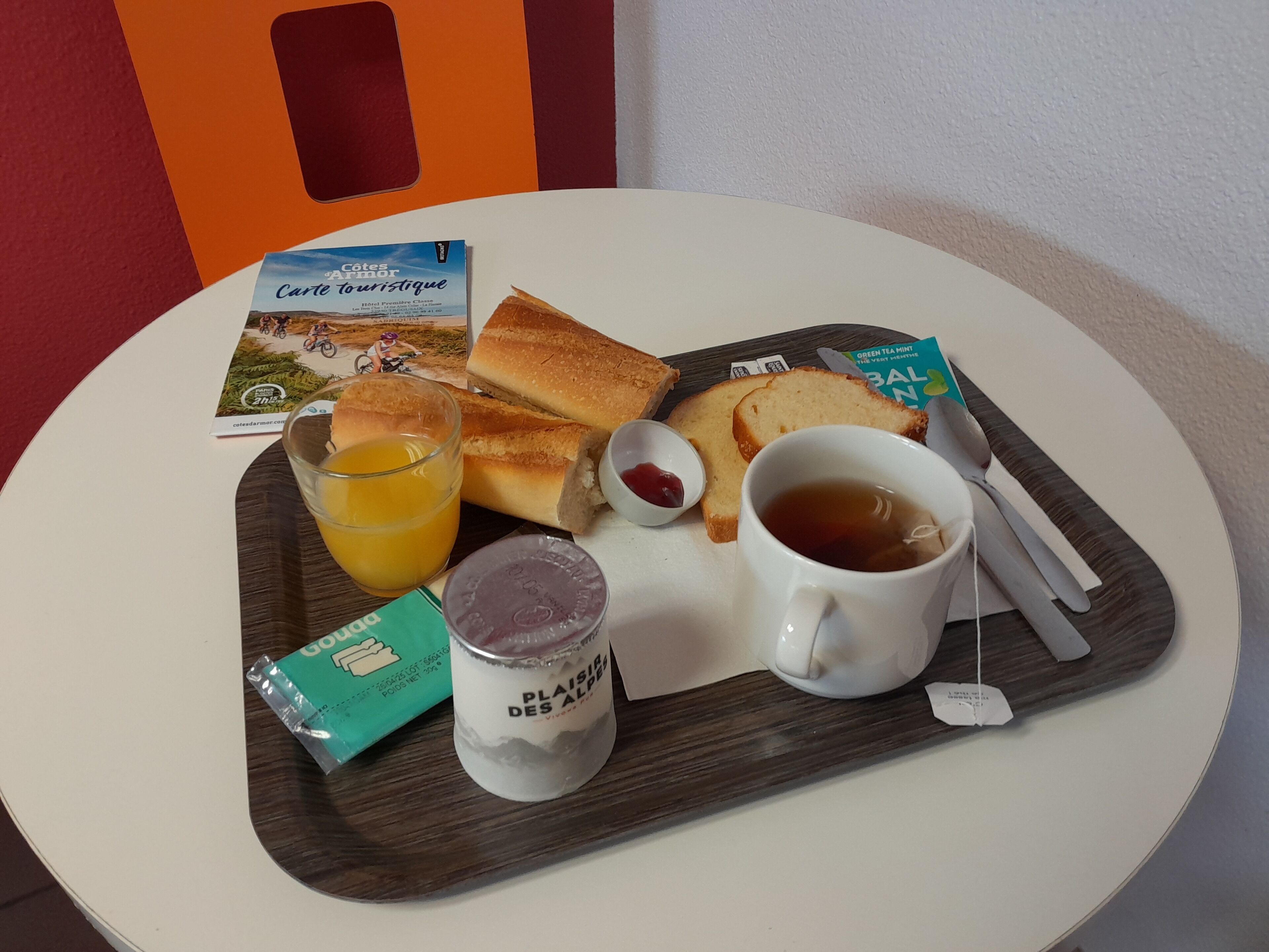 A breakfast tray with bread, butter, jam, tea, and juice on a white table.