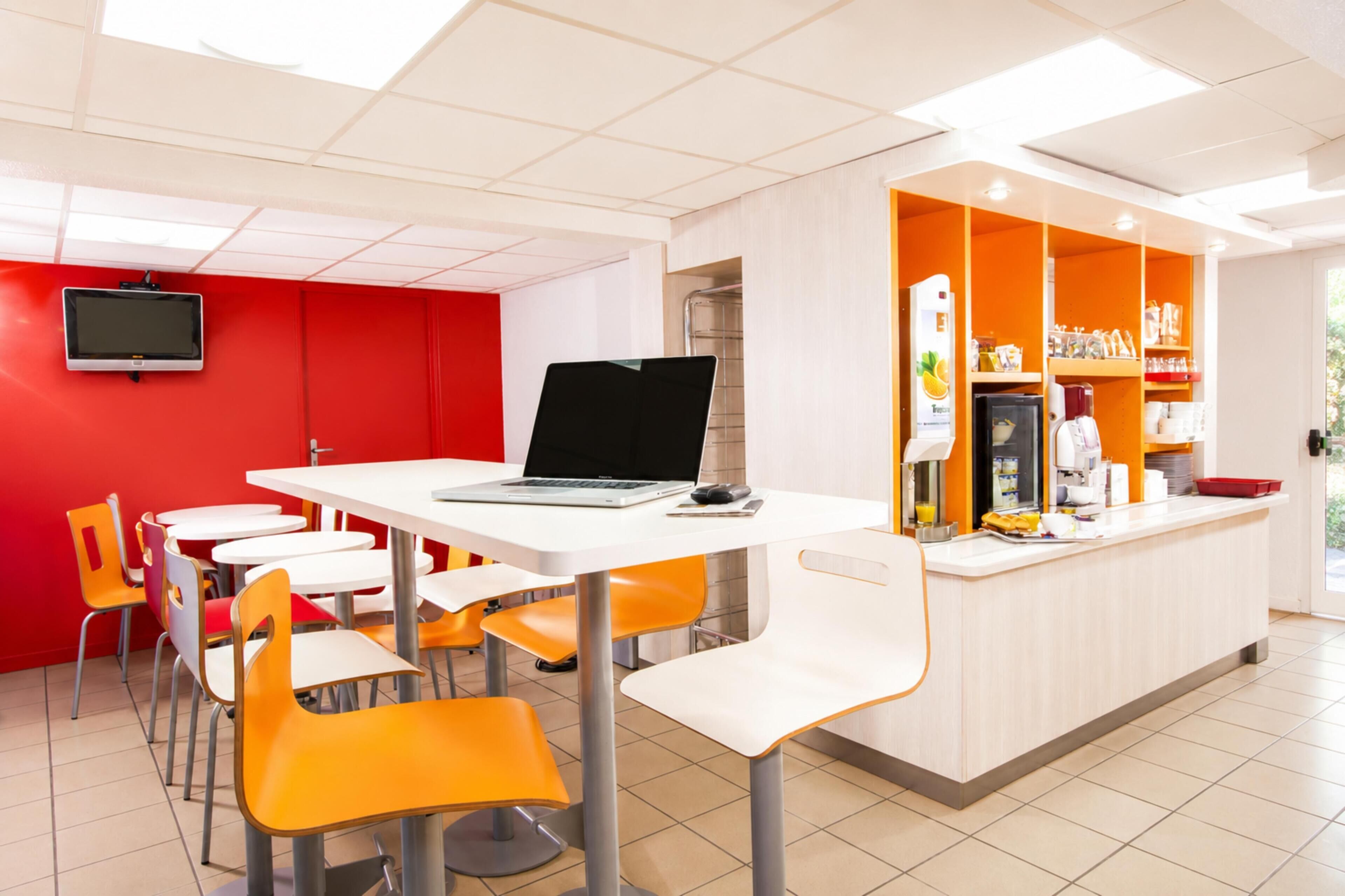 A modern cafe with a white counter, orange chairs, and a red wall.