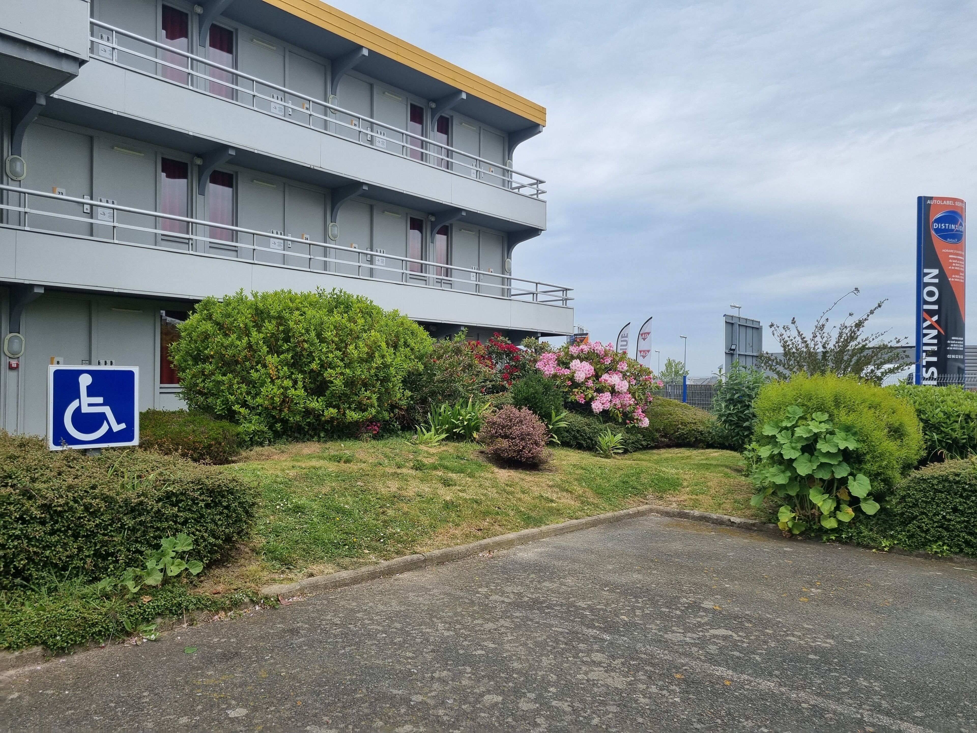 A modern building with a wheelchair-accessible entrance, a parking area, and a large sign for 'STINXION'.