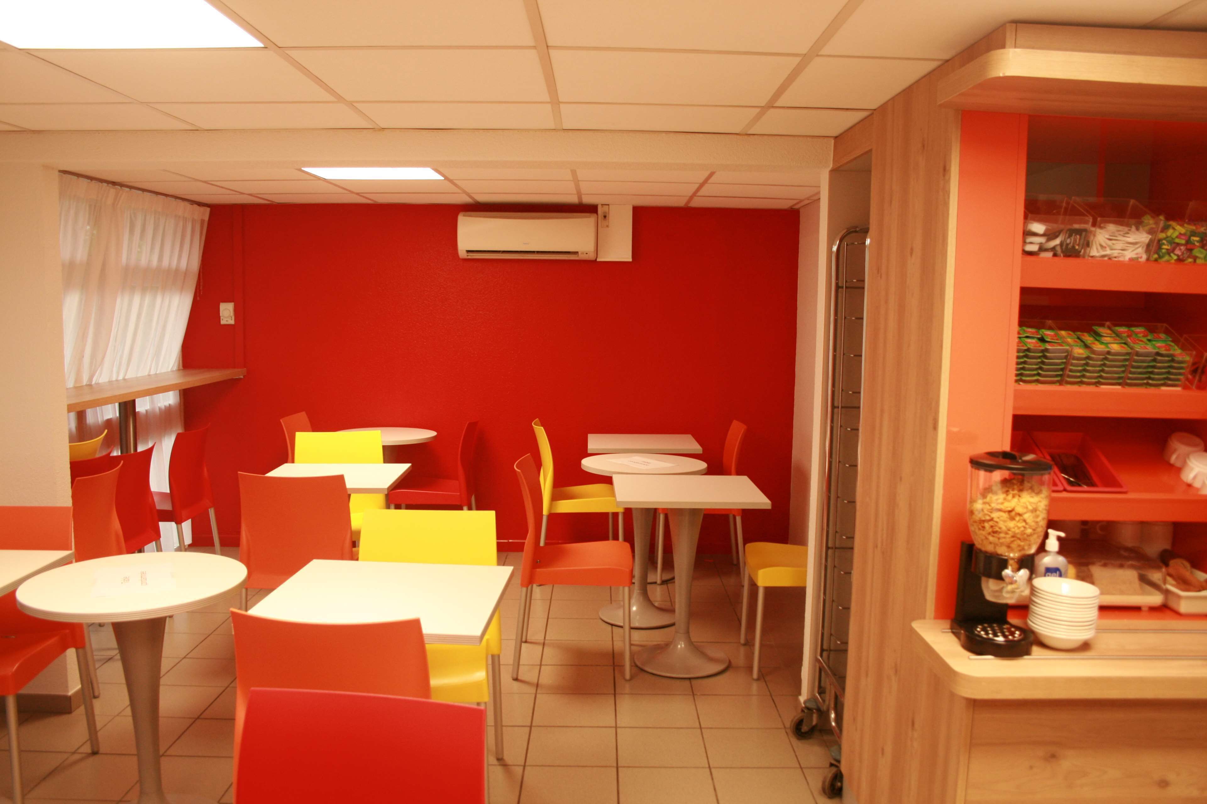 Ein lebhaftes Restaurant mit roten Wänden, gelben und orangen Stühlen und weißen Tischen.
