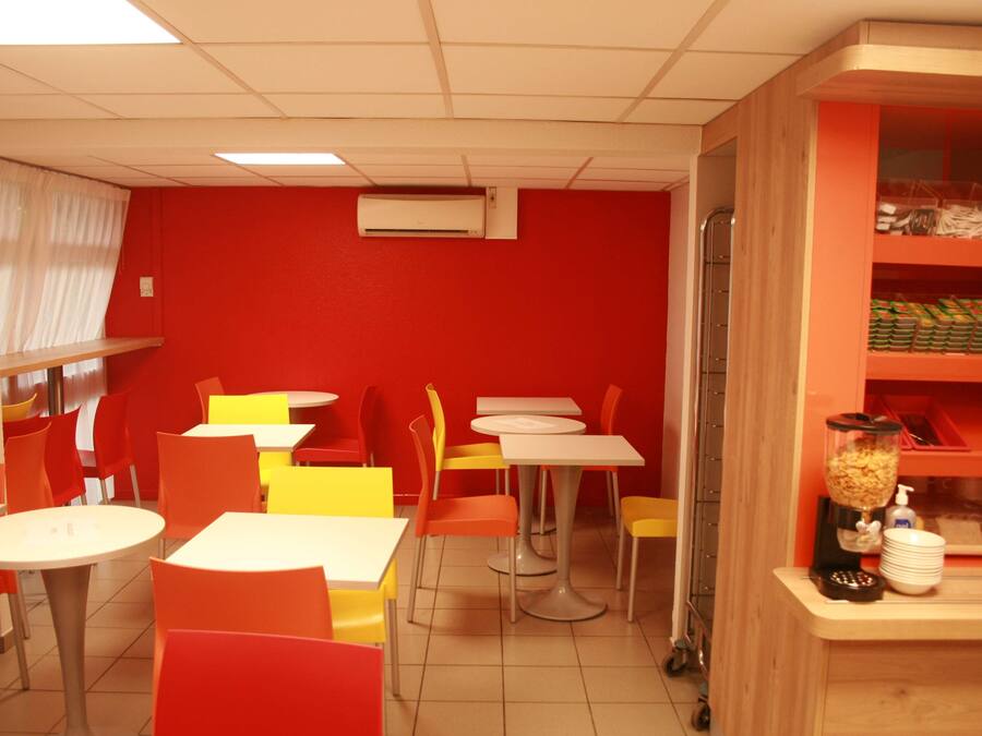Un restaurante de colores vivos con paredes rojas, sillas amarillas y anaranjadas, y mesas blancas.
