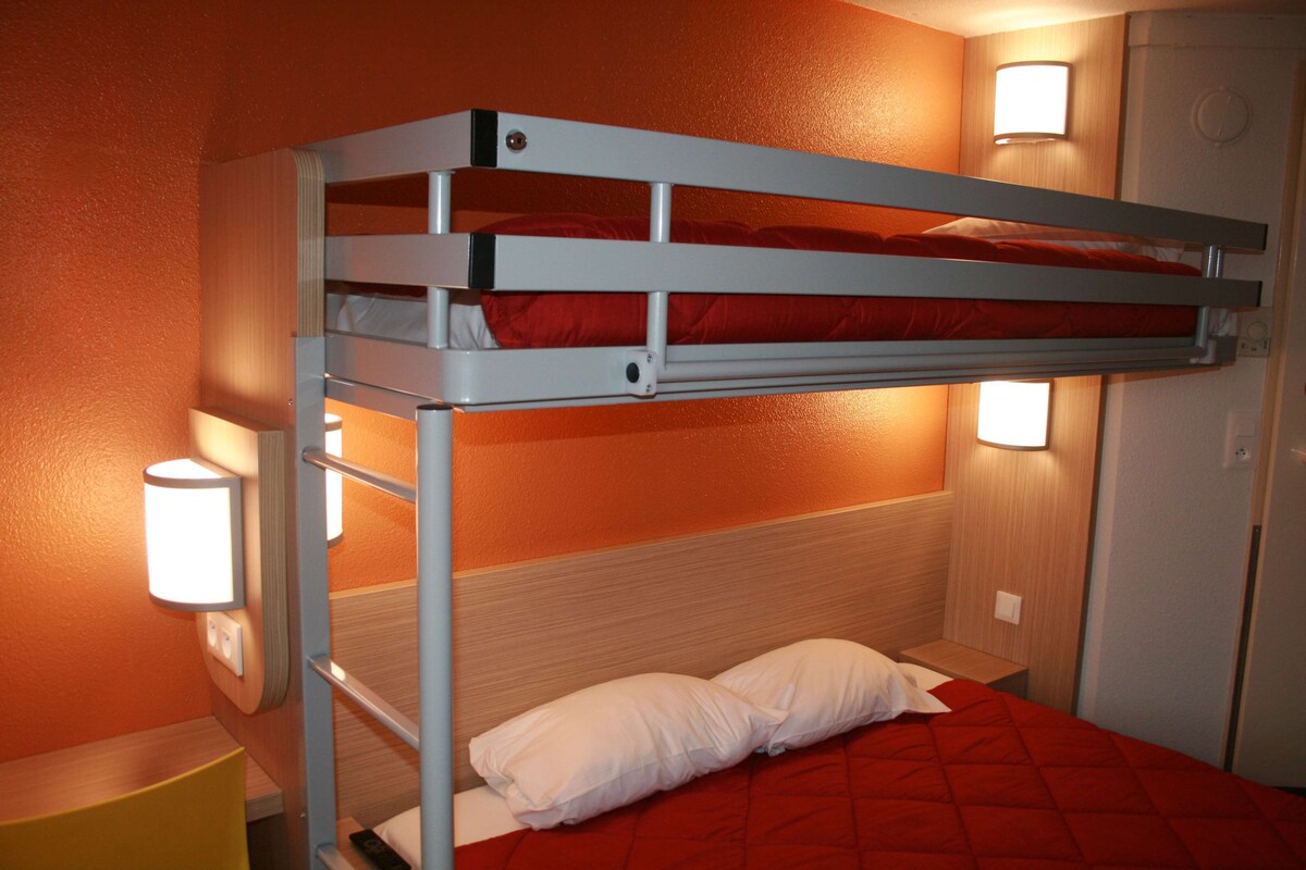 Una cama litera con dos almohadas, cabecero de madera y dos luces fijadas a la pared.