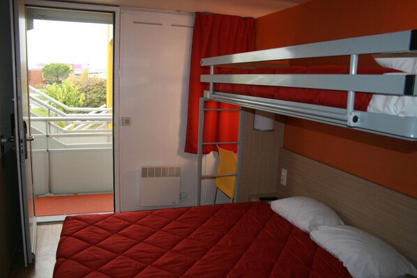 A room with a bunk bed, a red bedspread, a white pillow, a red curtain, and a yellow chair.