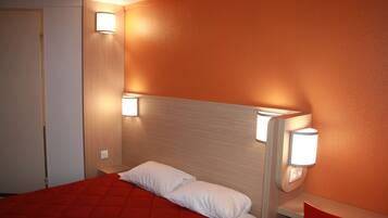 Habitación de hotel con colcha roja, almohada blanca y dos luces fijadas a la pared.
