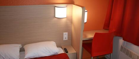 A hotel room with a bed, a desk, and a chair. There is a remote control on the desk.