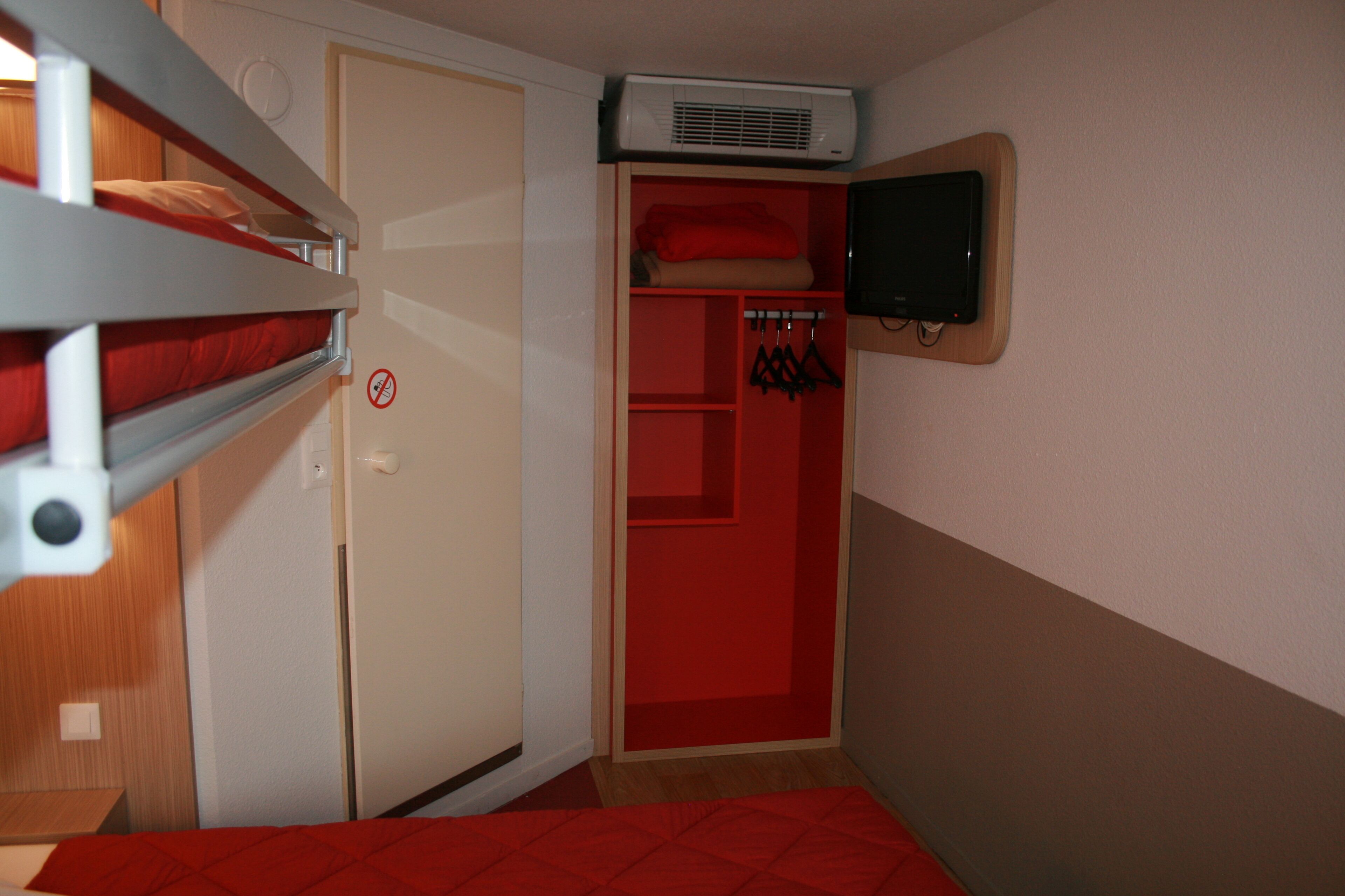 Una habitación con literas, un armario y un televisor montado en la pared.