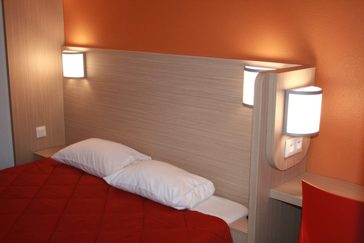 A hotel room with a bed, two bedside lamps, and a red chair.