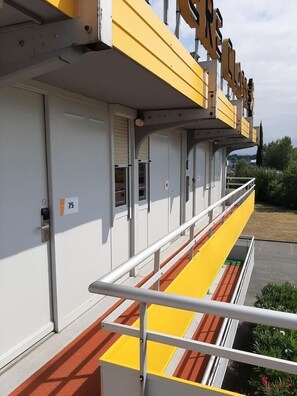 A building with a yellow and white facade, a balcony with a metal railing, and a sign with the number 75. - Premiere Classe Carcassonne (Carcassonne)