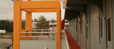 A corridor with a yellow structural element, a red carpet, and a view of buildings in the background.