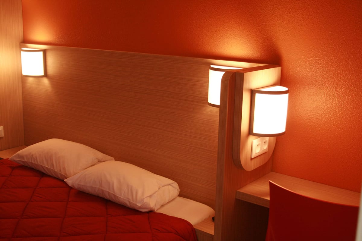 A hotel room with a wooden headboard, two bedside lamps, a red bedspread, and white pillows.