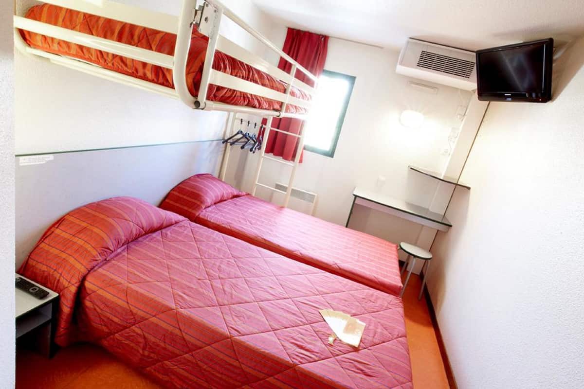 Une petite chambre avec des lits superposés, un bureau et un téléviseur.